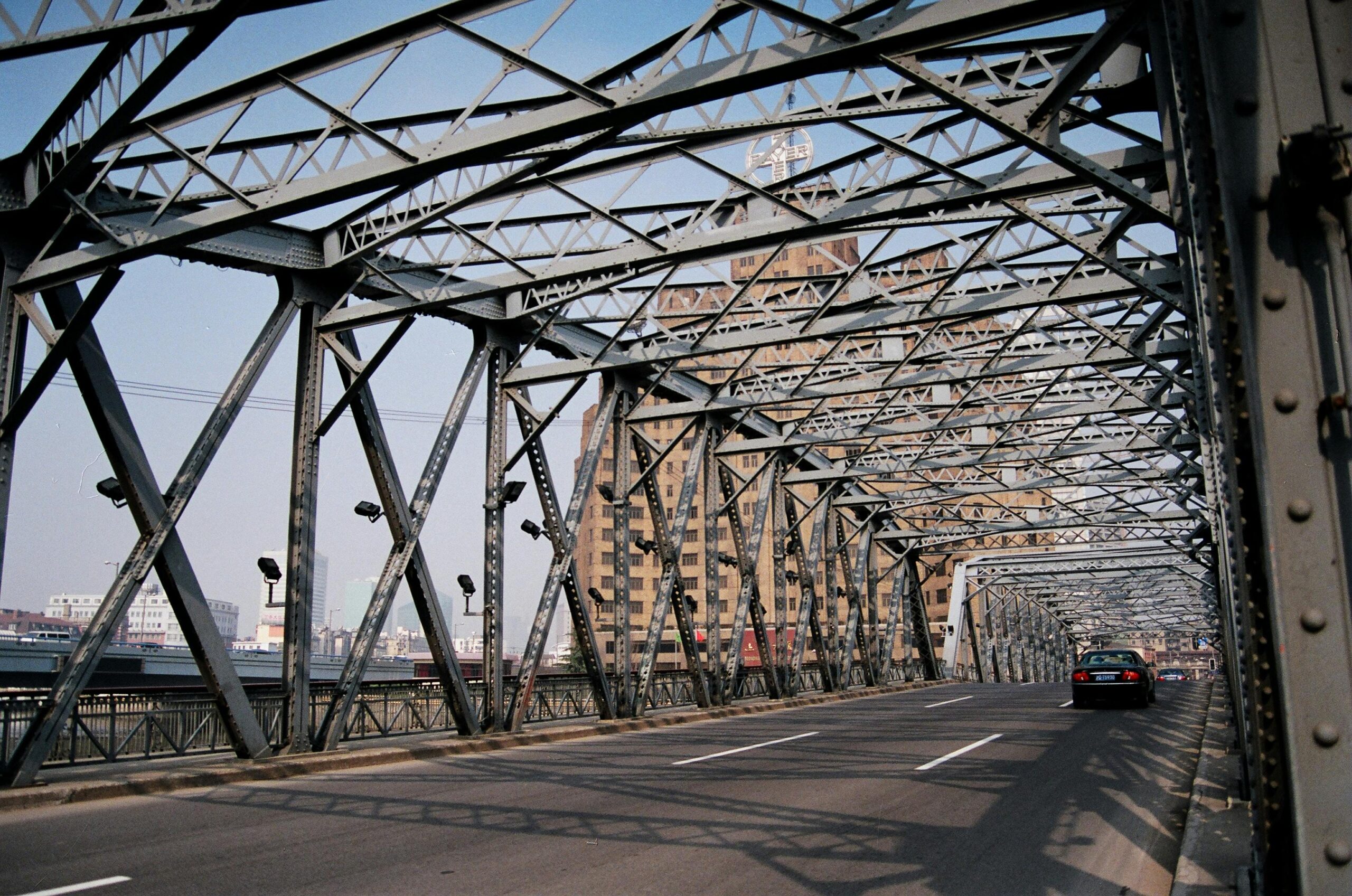 Photo of a steel bridge in an urban setting with a cityscape in the background.